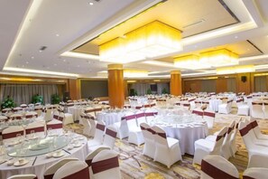 A banquet hall with round tables, white chairs, and a carpeted floor. - Camellia Hotel (Kunming)
