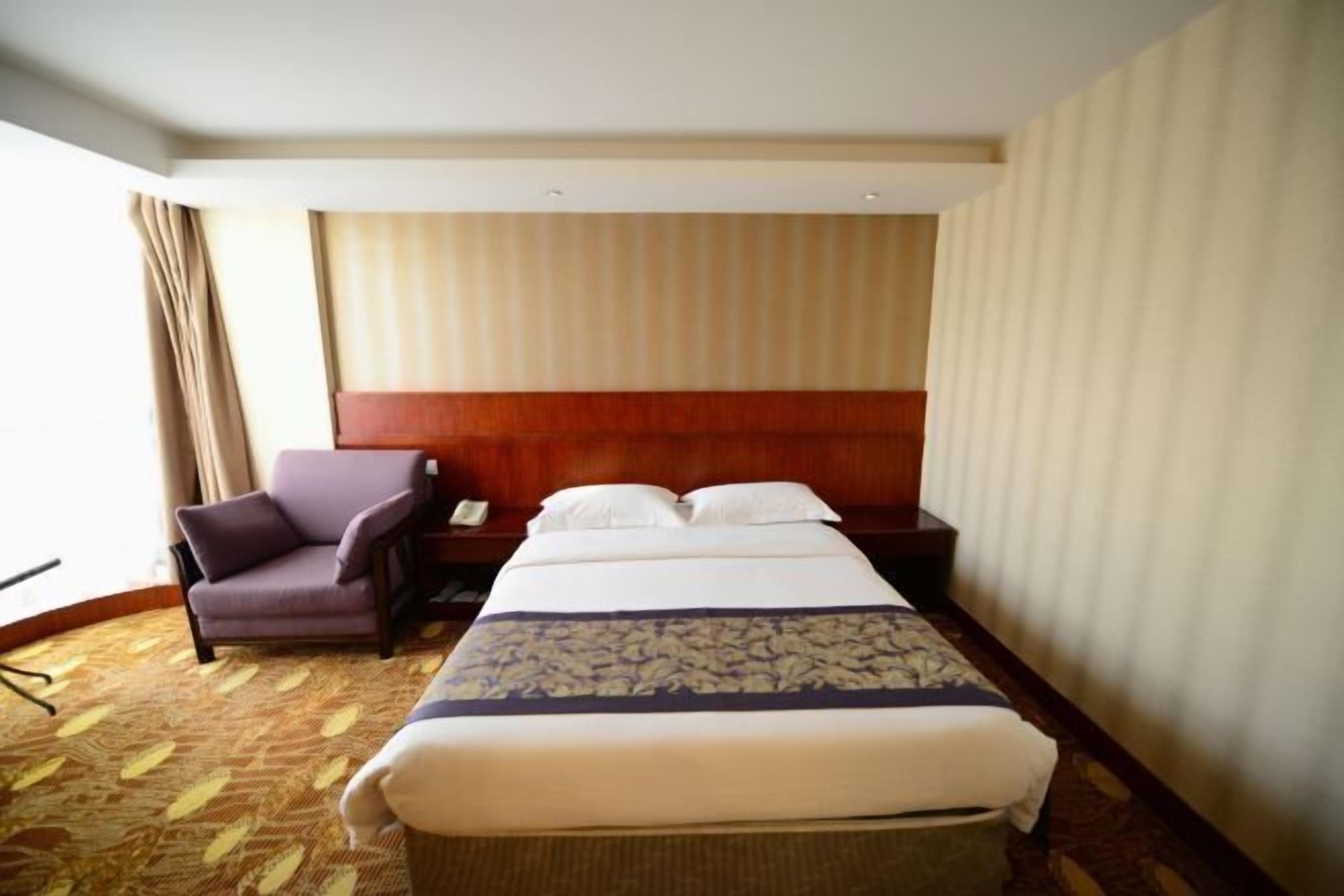 A hotel room with a large bed, a chair, a nightstand, and a window with curtains.