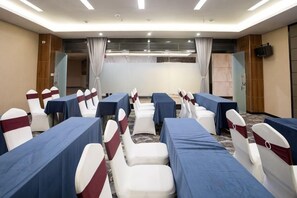 A conference room with rows of tables and chairs, a large screen at the front, and a wooden panel wall. - Camellia Hotel (Kunming)