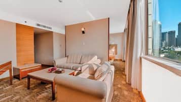 A modern hotel room with a sofa, a small table, and a view of the city skyline through large windows.