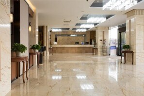 Un vestíbulo de hotel con mostrador de recepción, suelo de mármol y plantas en macetas.