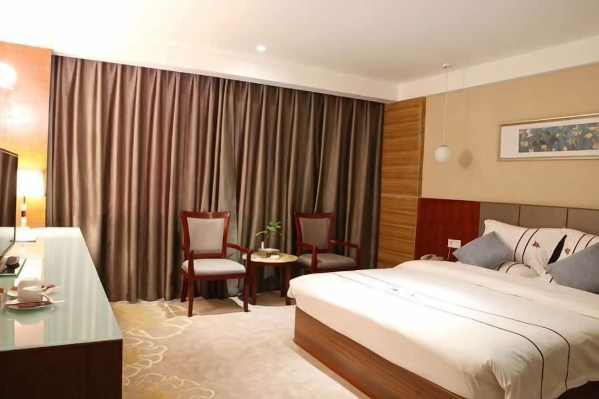 Une chambre d’hôtel avec un lit, deux chaises, un bureau et une grande fenêtre avec des rideaux.