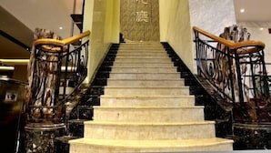 A marble staircase with black railings and wooden handrails, leading to a wall with Chinese characters. - Camellia Hotel (Kunming)