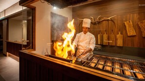 Un chef cuisinant au-dessus d’une flamme dans une cuisine moderne, avec des éléments en bois et des ustensiles de cuisine en bois suspendus.
