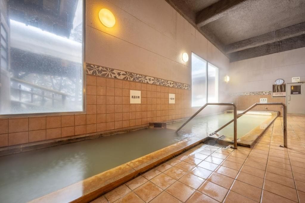 Un espace de baignade dans une source thermale, avec des murs carrelés, un banc en bois et une horloge au mur.