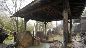 Une structure rustique en bois, dotée d’un sol en pierre et d’un toit en bois, entourée de formations rocheuses naturelles et d’une clôture en bois.