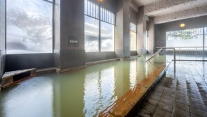 Une grande baignoire d’eau chaude intérieure, avec des murs carrelés et une plateforme en bois.