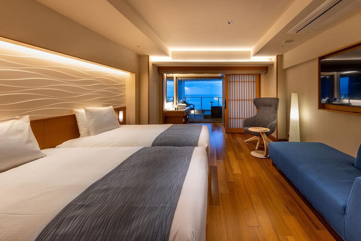 Ein Hotelzimmer mit zwei Betten, einem Schlafsofa, einem Sessel, einem Fernseher und Meerblick.