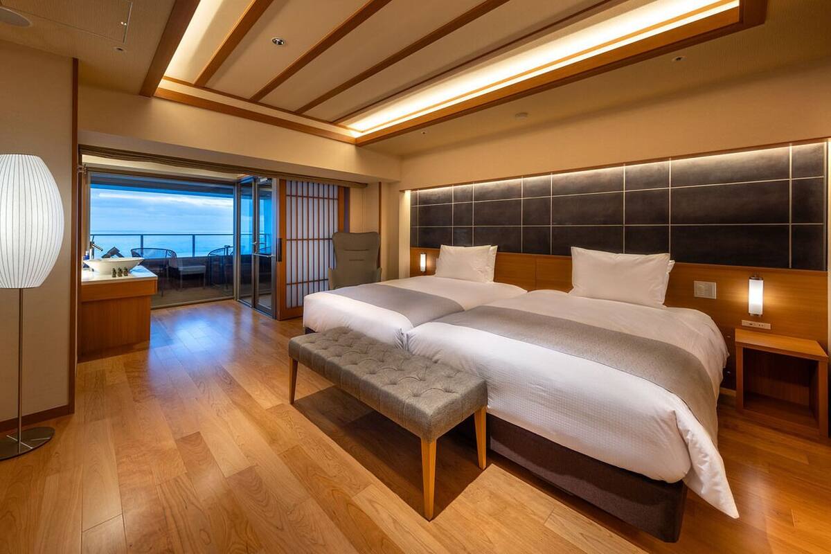Ein modernes Hotelzimmer mit einem großen Bett, einer Bank, einem Nachttisch und Meerblick.