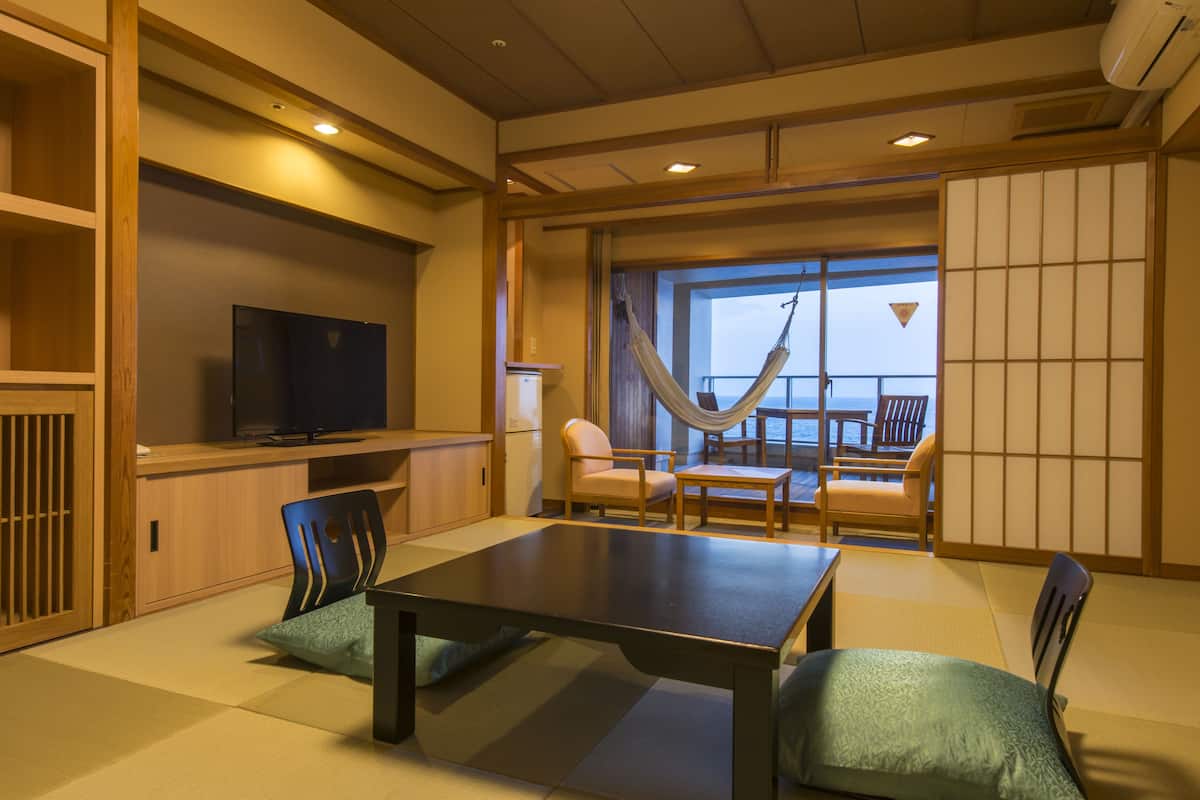 Ein traditioneller japanischer Raum mit Tatami-Boden, einem niedrigen Tisch und einem Fernseher auf einem Holzkasten.