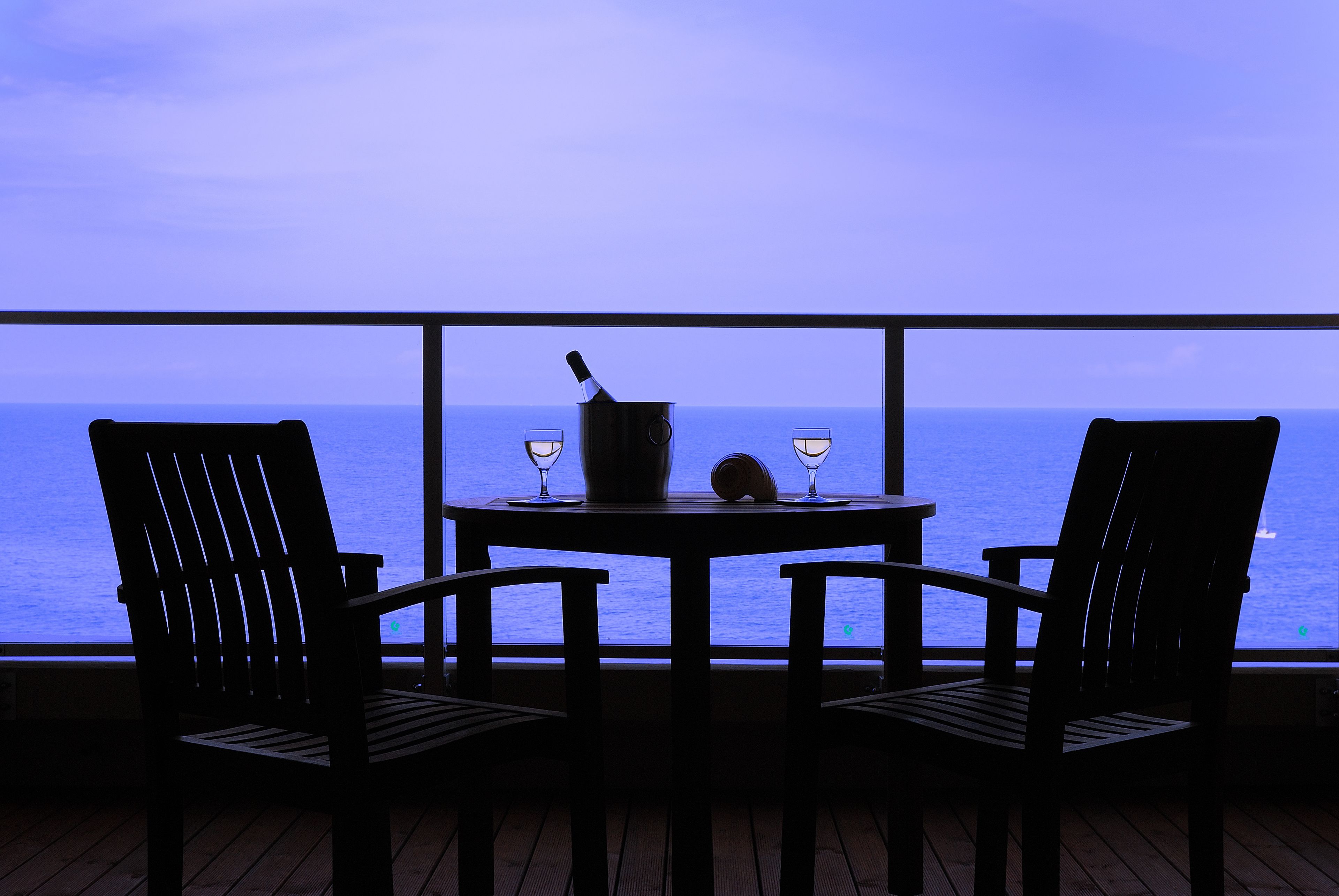 A balcony with two wooden chairs and a small table, overlooking a body of water.