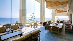 Amplio espacio interior con grandes ventanales con vistas al mar, amoblado con diversos conjuntos de asientos y mesas.