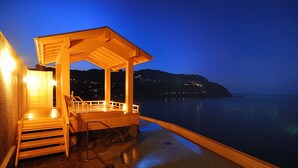 Una terraza de madera con zona de estar cubierta que da a un cuerpo de agua por la noche.