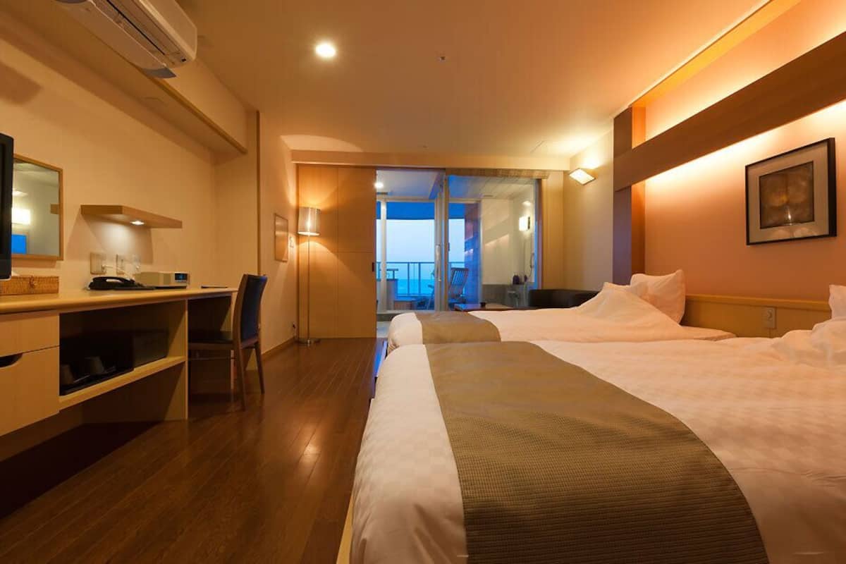 Ein Hotelzimmer mit Bett, Schreibtisch mit Computer, Fernseher und einem Balkon mit Blick.