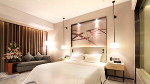 A modern hotel room with a large bed, a sofa, a nightstand, and a wall-mounted artwork. - Shuidu Holiday Hotel (Shenzhen)