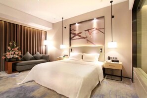 Una habitación de hotel moderna con una cama grande, un sofá, una mesita de noche y una obra de arte colgada en la pared.