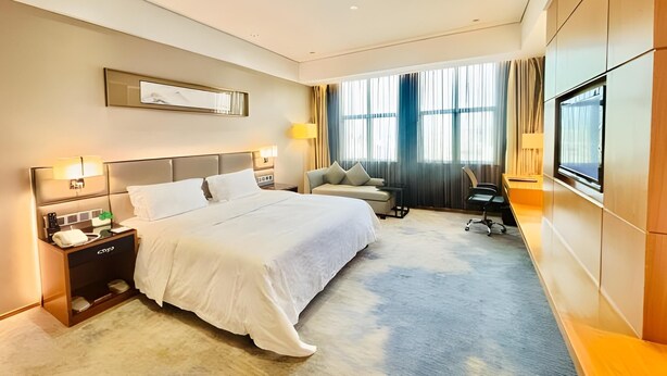 A hotel room with a large bed, bedside tables, a desk, a chair, and a TV mounted on the wall. - Shuidu Holiday Hotel (Shenzhen)
