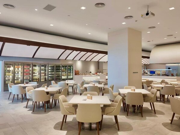 A modern dining area with tables and chairs, a bar area, and a refrigerated display case with beverages.