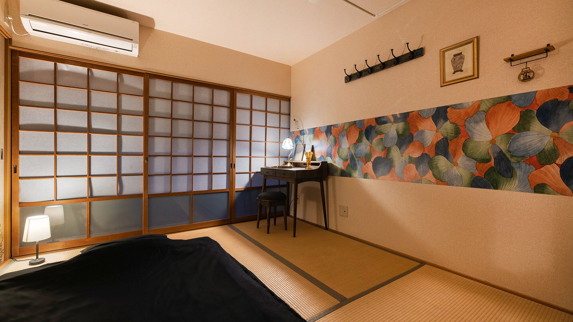 A traditional Japanese room with tatami flooring, a shoji screen, a desk with a lamp, and a colorful floral wall.