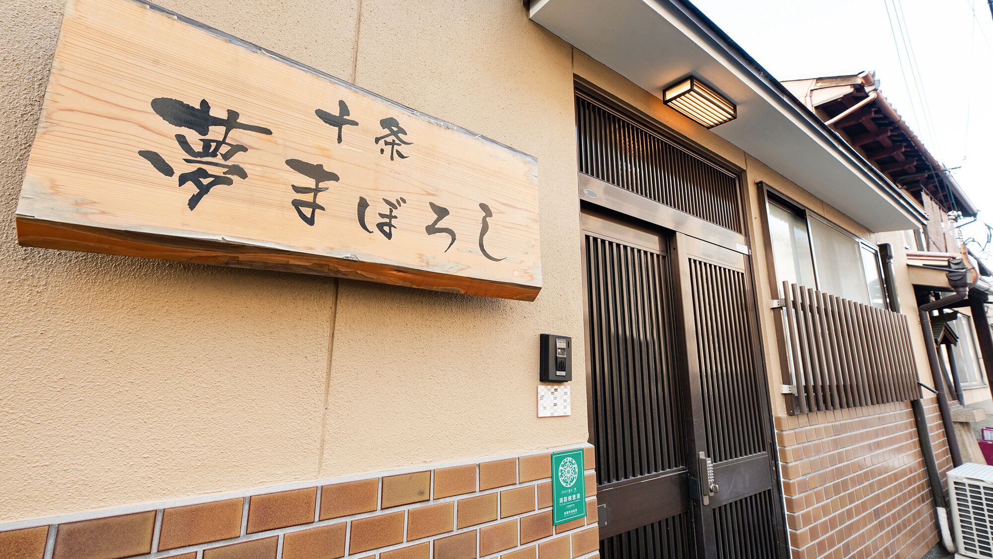 Un edificio con un letrero de madera que muestra caracteres japoneses, una reja metálica y un muro de ladrillo.