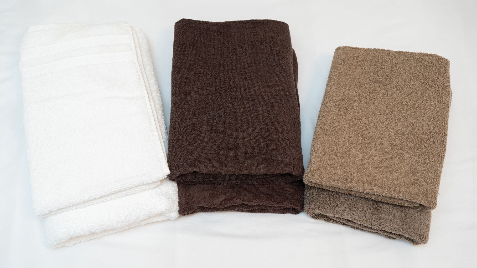 Three folded towels in white, dark brown, and light brown colors.