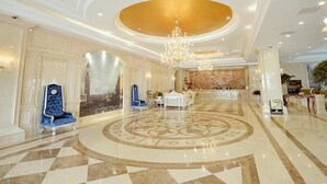 Un vestíbul ampli amb un gran candelabrum, un centre decoratiu circular al terra i una taula de recepció.