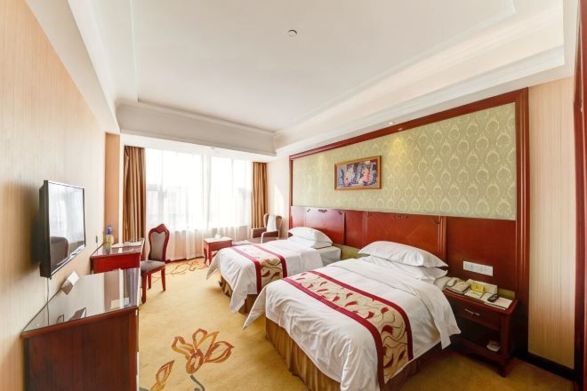 A hotel room with two beds, a TV, a desk, and a chair.
