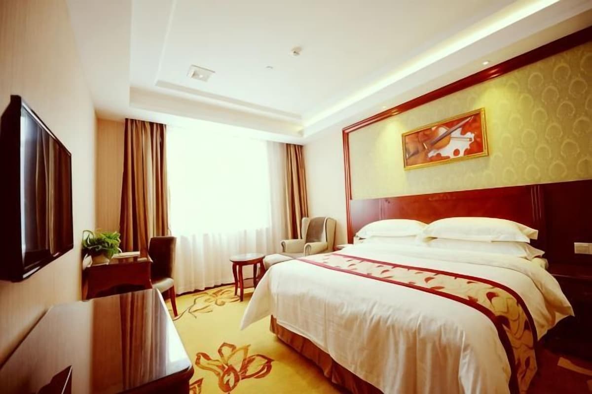 A hotel room with a bed, a TV, a desk, and a chair.
