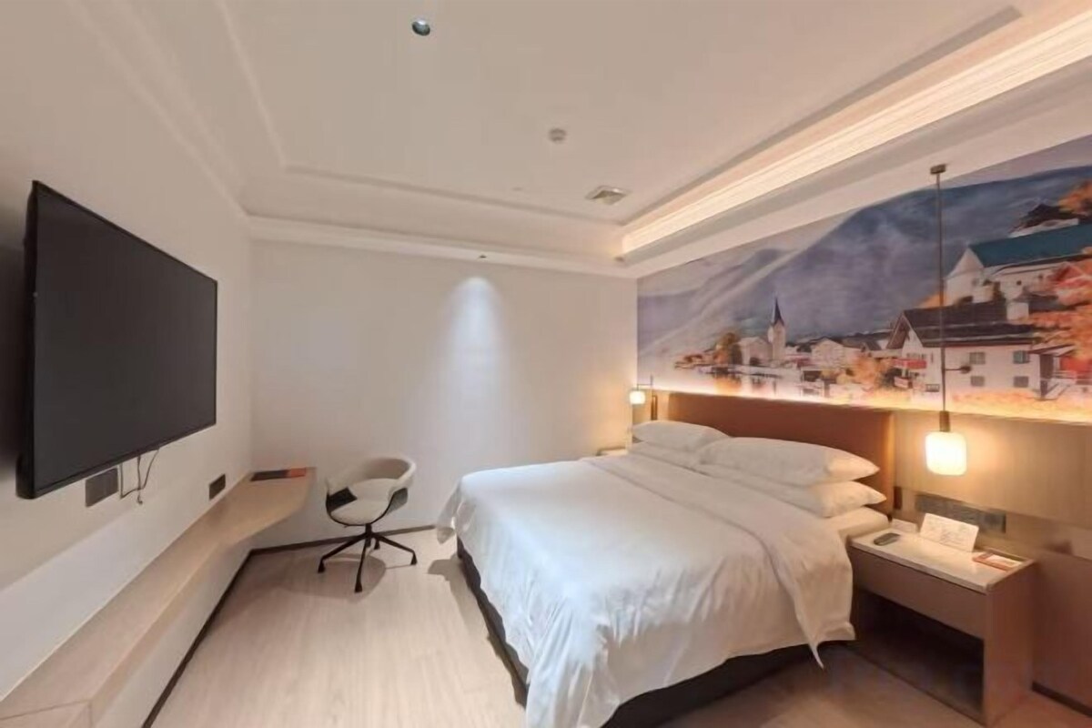 A hotel room with a bed, a desk, a chair, a flat-screen TV, and a wall mural.