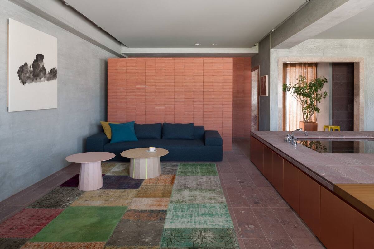 A modern living room with a sofa, two small tables, a colorful rug, and a kitchen area with a sink and plant.