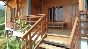 A wooden cabin with a porch, wooden stairs, and a bench. - Istana Petani Hotel (Sukapura)