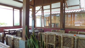A restaurant with bamboo furniture and large windows. - Istana Petani Hotel (Sukapura)