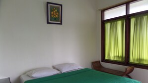Een enkel bed met een groene sprei, een houten stoel, een klein tafeltje en een raam met groene gordijnen.
