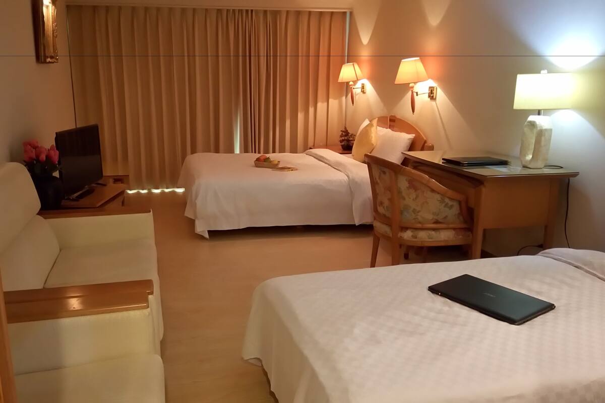 A hotel room with two beds, a desk with a lamp, a TV, and a chair.