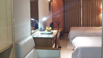 A hotel room with a desk, two beds, a chair, a mirror, and a lamp.