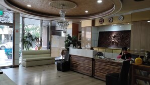 A hotel lobby with a reception desk, seating area, and a decorative ceiling.