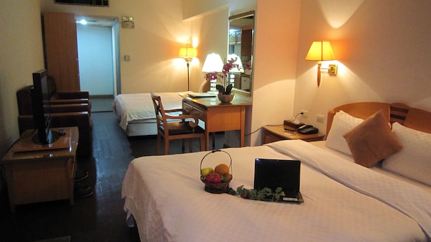 A hotel room with two beds, a desk, a chair, a TV, and a lamp.