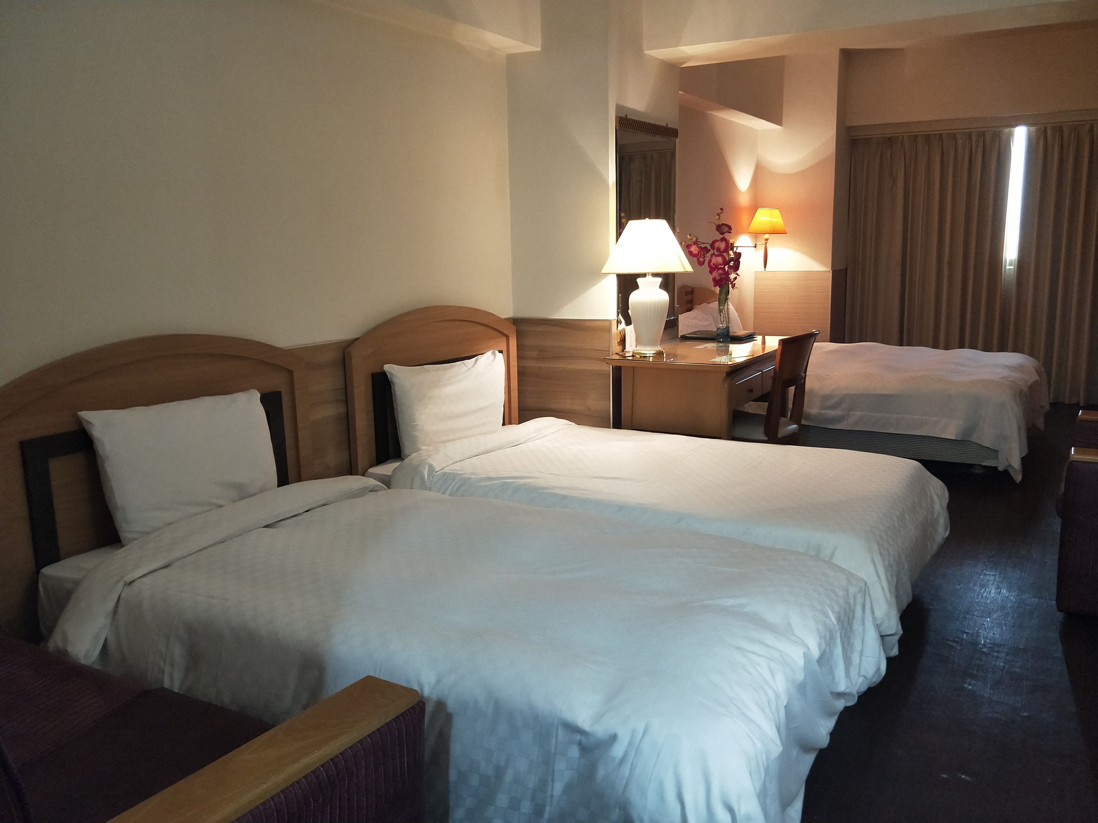 A hotel room with two beds, a desk with a lamp, a chair, and a mirror.