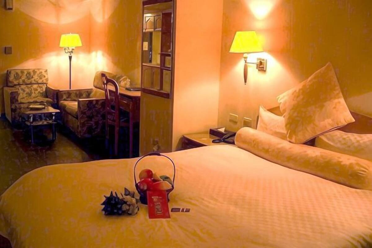 A hotel room with a bed, two chairs, a nightstand, a lamp, and a mirror.