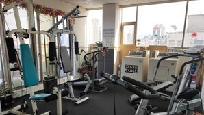 A gym with various exercise equipment, including treadmills and weight machines, and a view of the city through large windows. - Berkeley Hotels (Hsinchu)