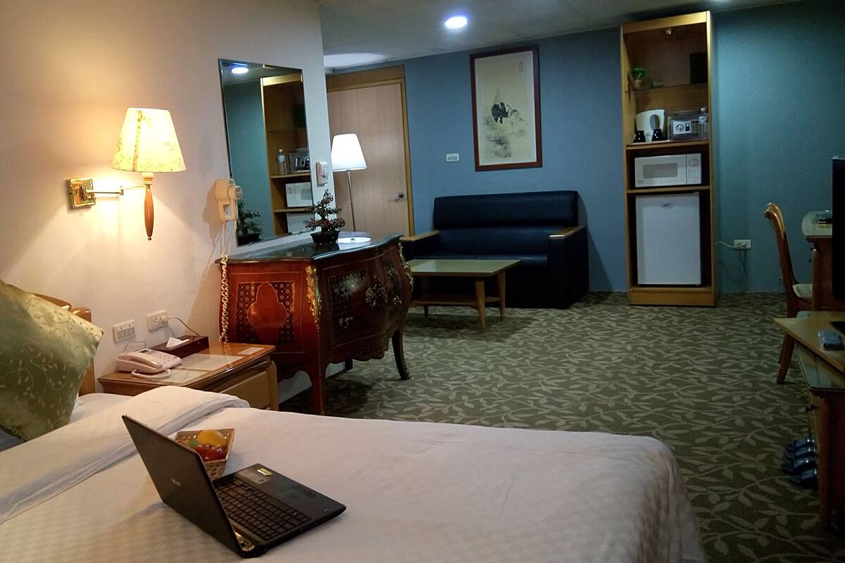 A hotel room with a bed, a desk, a chair, a sofa, and a small table.