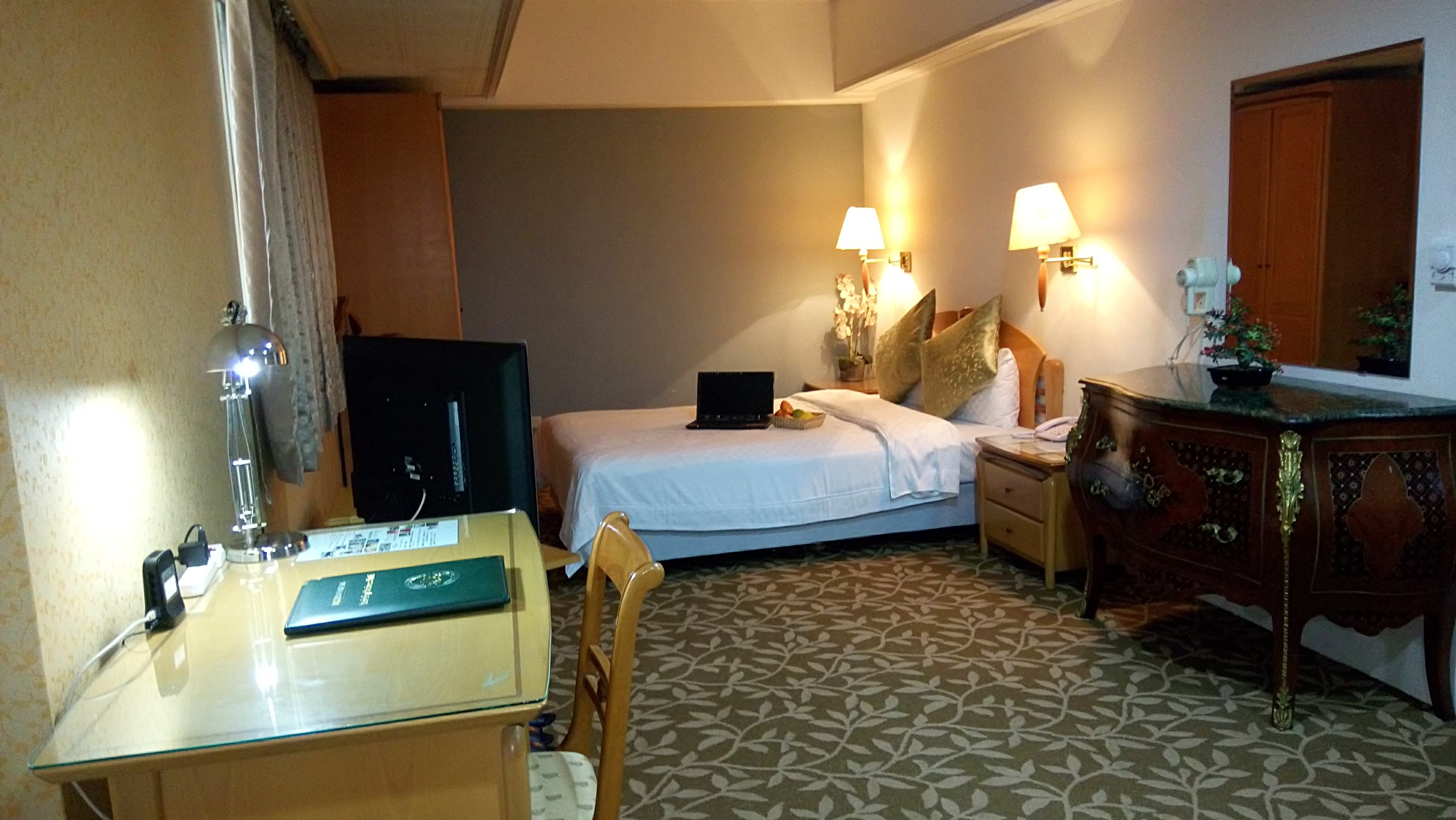 Una habitación de hotel con cama, escritorio, silla, lámpara y cómoda.