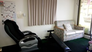 A room with a massage chair, a floral sofa, and a window with curtains. - Berkeley Hotels (Hsinchu)
