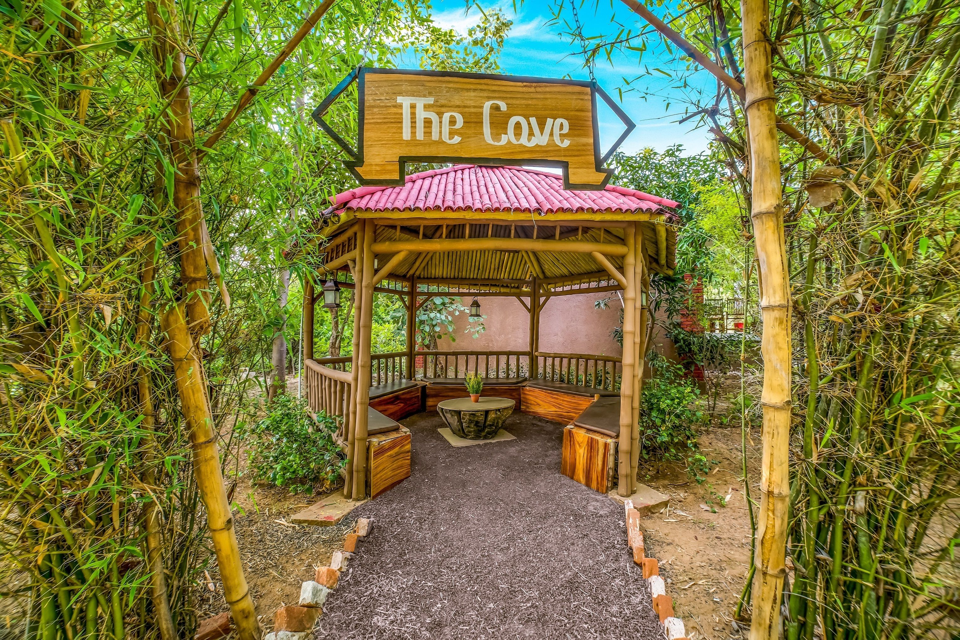 Un gazebo in legno con un tetto rosso, con l'indicazione "The Cave", circondato da bambù e vegetazione.