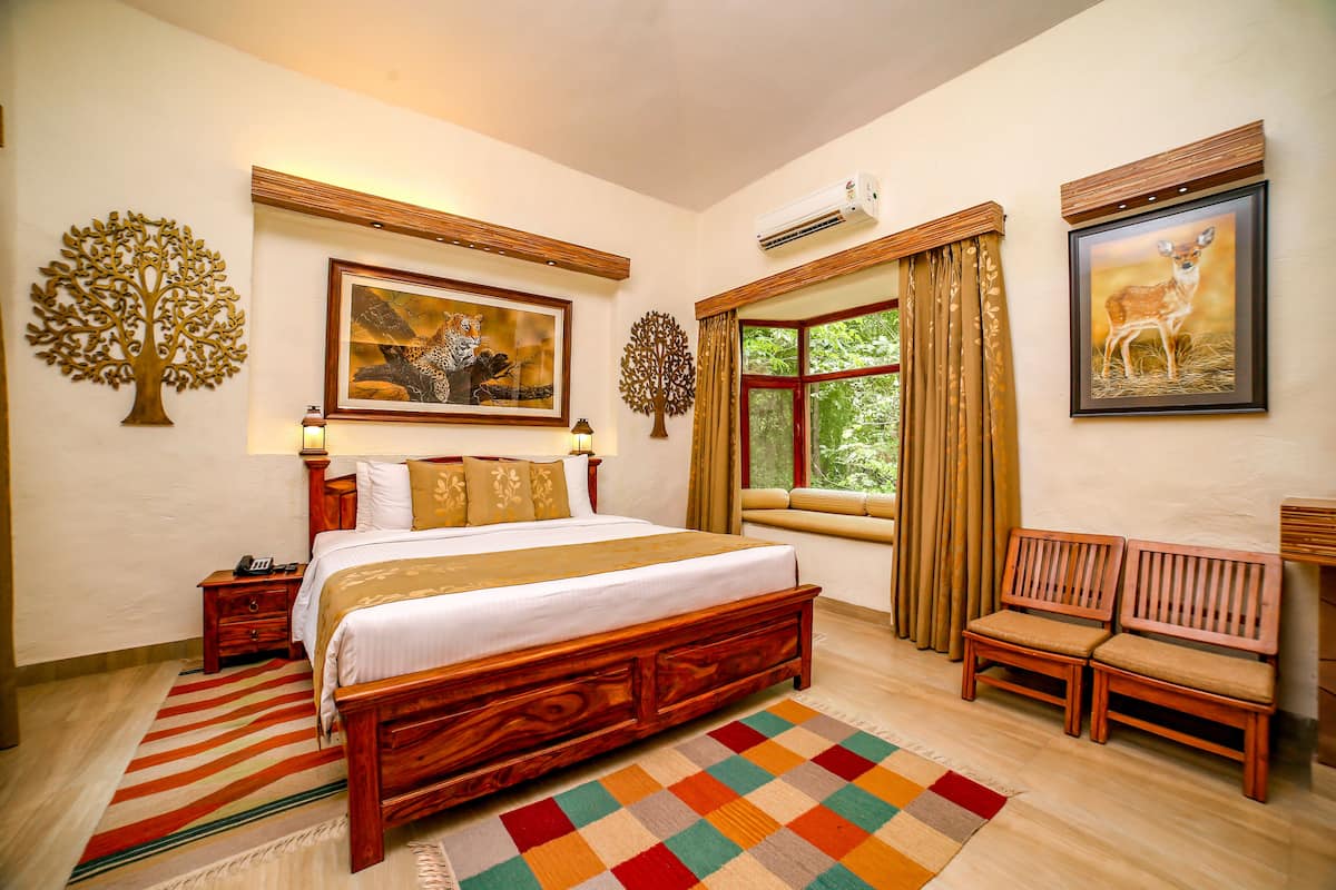 A bedroom with a large bed, a wooden bench, a window with curtains, and two wall-mounted air conditioners.