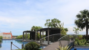 Un área de piscina con terraza de madera, zona de estar cubierta y un puente sobre la piscina.