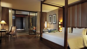 Habitación de hotel con una cama grande, una zona de estar con sofá y sillones, un escritorio con silla y una puerta de cristal que da a un balcón.