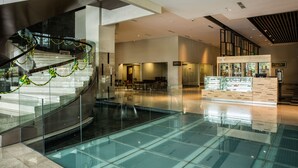 Un interior moderno con una escalera de fondo de cristal, una fuente central y una vitrina de panadería.