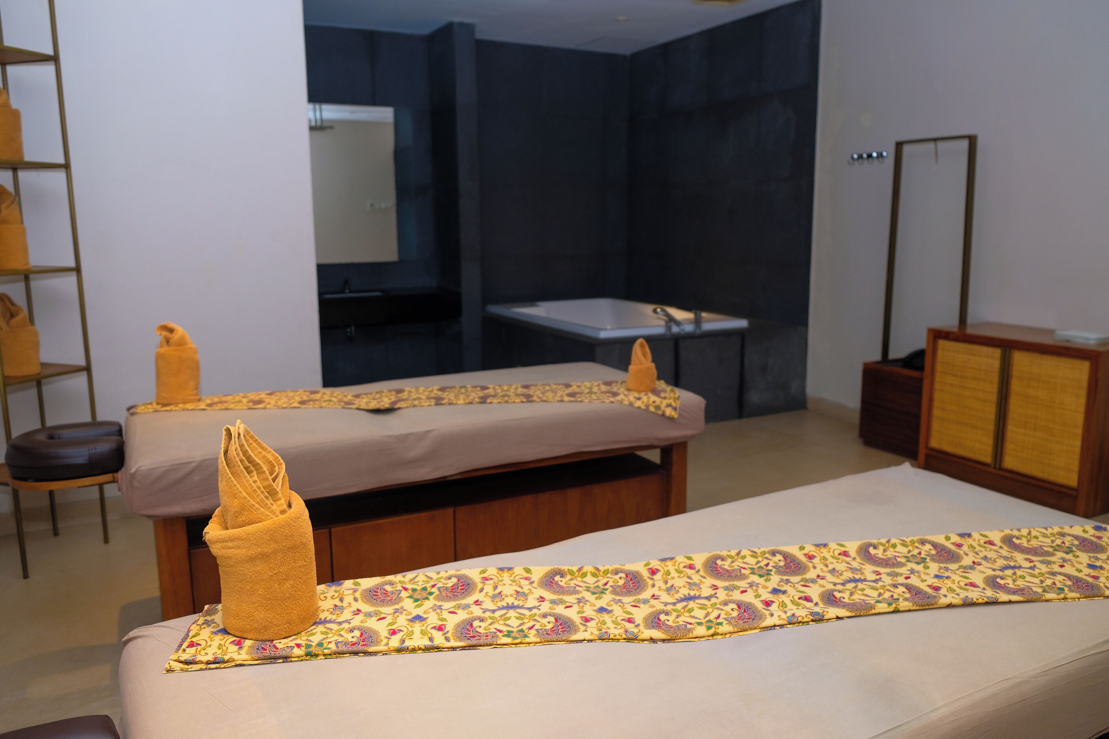 A room with two beds, a small table, a mirror, and a dark wall.