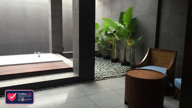 Un baño moderno con una bañera, una silla de mimbre y plantas verdes grandes.